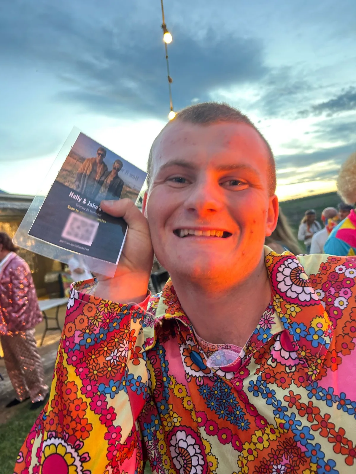 A guest at a 21st holding up the printed GuestCam card with its QR code, at sunset.